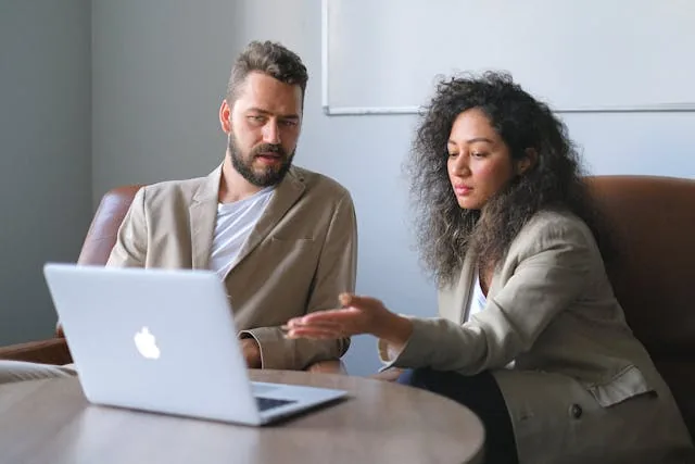 A man and a woman discussing something in front of a laptop